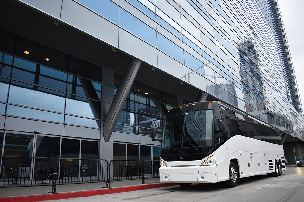 White charter bus on the street next to red curb below a building with blue and white stained windows