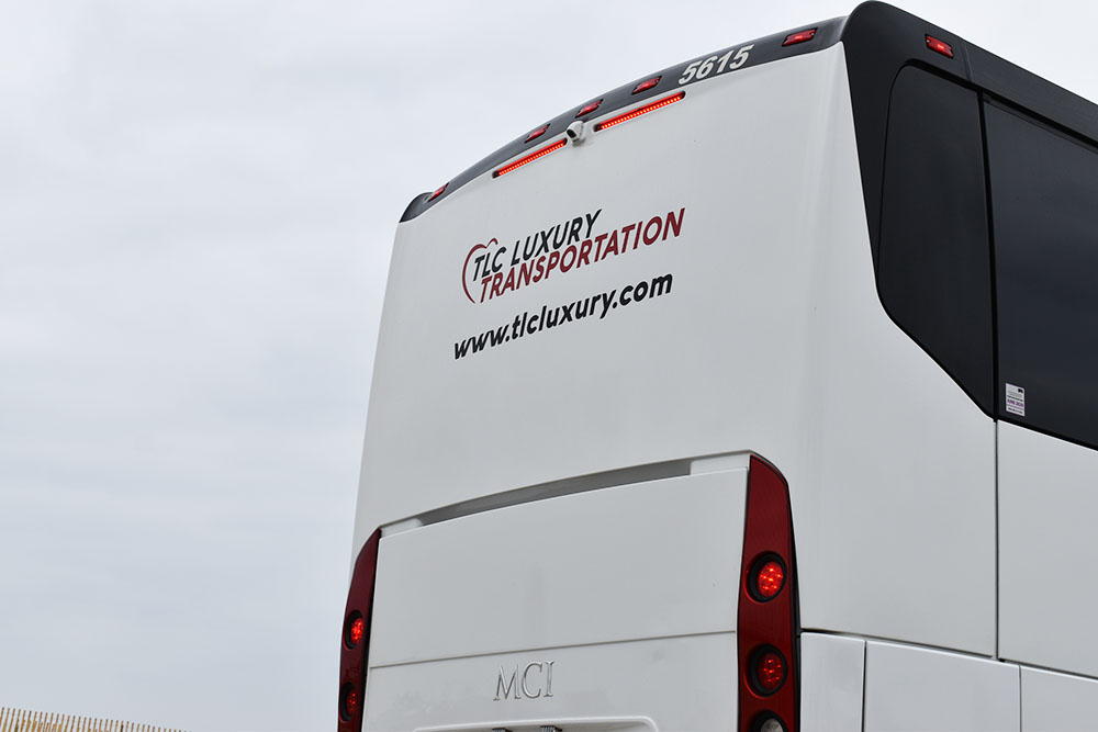 Posterior of white charter bus with logo reading 'TLC Luxury Transportation' and storm clouds above vehicle