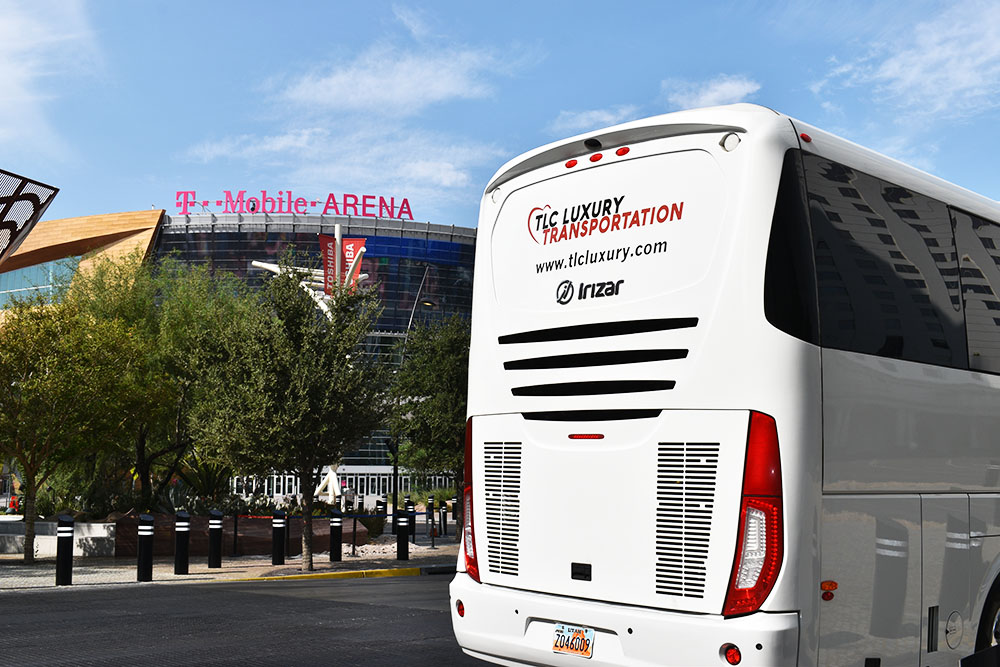 Back of white tour bus with logo reading 'TLC Luxury Transportation' with green trees and blue skies in the background.