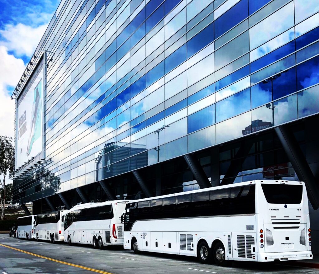 Blue and white patterned building with clouds in reflection and white los angeles charter buses below parked on the street