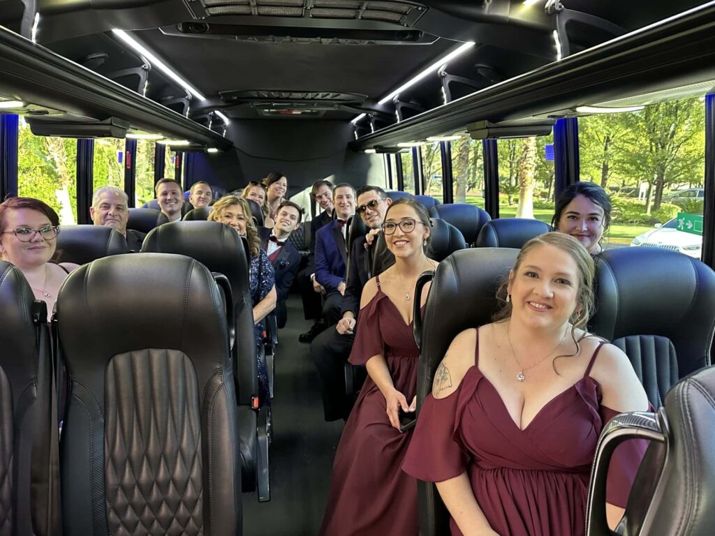 Bridesmaids wearing maroon dresses and groomsmen riding in bus with black leather seats