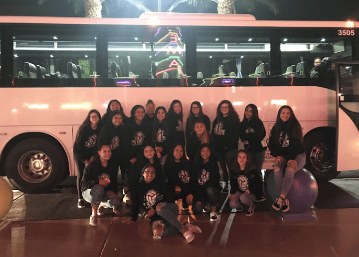 Female students in black sweatshirts posing in front of white bus